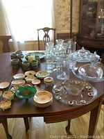 Wide shot showing assortment of glassware, ceramic cups, bowls and china trinket dishes laid out on wooden table