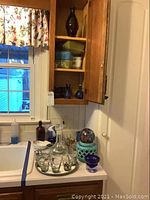 Photo of kitchen counter interior with clear etched glass decanter, six matching etched glasses on tray, blue glass votive holder, multicolored glass ball, blue glass bottles, ceramic pitcher, and ceramic lantern candle holder.