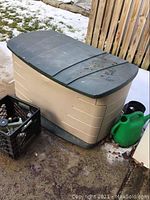 Rubbermaid outdoor storage box with dark green lid, green watering can, and black crate.