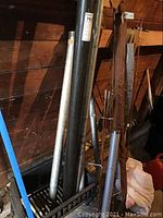 Multiple fly rods leaning against wall beside black and silver metal tubes