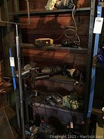 Shelf with multiple black and decker power tools including drills, saws, and a sander or drill with cords and handles, showing general condition and different tool types.