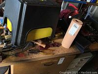 Black and yellow storage bins, paper towel roll, various hand tool handles on wood cabinet surface.