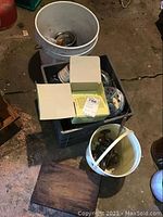 Overview photo showing buckets and crates with fishing reels and metal weights along with a wooden box on the floor.