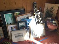 Photo showing multiple framed art pieces and mirror leaning against a wall on a carpeted floor