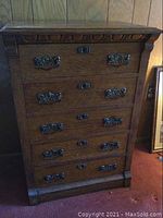 Full view of the vintage wooden chest of drawers showing the five drawers with ornate metal handles and carved trim.