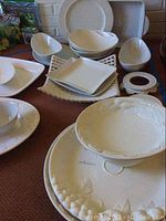 Multiple white ceramic and porcelain dishes of various shapes and sizes arranged on brown carpet. Includes bowls, plates, and platters with embossed and textured designs.