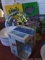 Photo showing white ceramic bowls stacked, boxed set of four wine glasses, decorative crab wall art, and metal platters with crab designs.