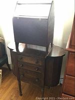 Sewing stand placed on top of the sewing cabinet showing front drawers and hinged side doors of cabinet.