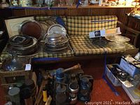 Front view of mid century modern sofa with wooden frame and yellow-green plaid cushions, surrounded by miscellaneous household items.