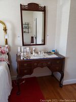 Front view of vanity table with five drawers, sitting on wood floor by wall with other furniture visible