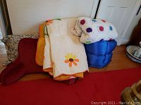 Two quilts, one with floral prints and one handmade crochet, stacked on a blue sleeping bag and pillows behind.