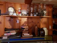 Wide shot of shelf with clocks, books and stoneware jugs and crocks on wood-paneled wall