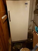 Full front view of white upright Signature freezer with vertical handle, placed on dark floor in basement environment.