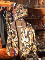 Photo of camo hunting jacket with zipper, elastic cuffs and bottom, and camouflage pattern with brown, tan, and black colors.
