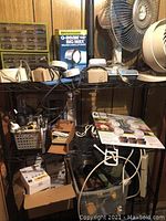 Metal shelving with multiple electrical items including timers, a spotlight box, fans, flashlights, and various hardware pieces