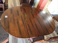 Top-down view of solid wood oval dining table with walnut stain finish, showing wood grain and one folding leaf in the center.
