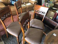View of four solid wood dining chairs with brown cushioned seats arranged in a semi-circle, highlighting chair backs with lattice cutout detail.