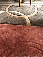 Close-up photo showing part of the floor rug with brown and reddish colors and circular design.