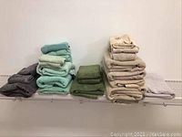 Stacks of towels in grey, green, taupe, and beige colors arranged on white wire shelving.