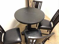 Four black pub style chairs and round black table arranged in a corner.