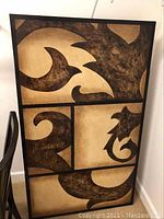 Front angled view of large abstract wall art piece showing swirling brown and black shapes on beige canvas with black section dividers.