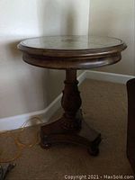 Full view of the round parlor table showing the wooden pedestal base and table top silhouette against a corner wall.