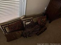 Several gold colored satin decorative pillows arranged side by side on floor against wall and baseboard