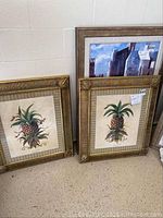 Two framed pineapple prints with gold-toned ribbed frames and glass, each showing detailed pineapple botanical artwork and artist signature B. Sikes.