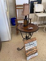 Photo of side table with metal legs and faux wood top, small lamp on table, and wooden wall art placed in front.