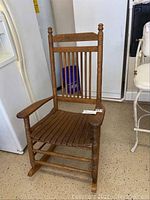Front angle view of a wooden rocking chair showing the spindle backrest, slatted seat, and armrests.