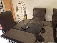 Side view of metal bird sculpture and abstract windy tree sculpture on table