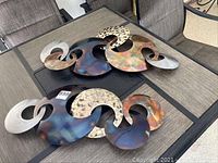 Photo showing the two abstract metal wall decor pieces placed on a table, highlighting their swirling shapes and varied metal finishes.