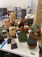 Candles, ceramic bird figurines in green, and various candle holders arranged on a white tabletop.