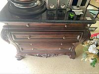 Front view of wooden dresser with black ceramic top showing carved details and drawer knobs.