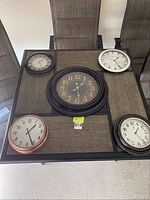 Top down view of five wall clocks arranged on a table showing different sizes and styles.