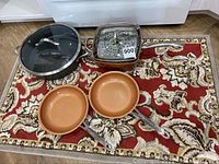 Wide angle photo showing all four pans: large black Calphalon pan with glass lid, Copper Chef square pan with steamer insert, and two small copper-colored Gotham Steel frying pans.