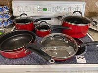 Red Cuisinart pots and pans set on stove with glass lids and black handles showing different sizes of pans and pots.