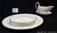 Five pieces of white Wedgwood fine china including two oval serving plates with gold trim, a gravy boat with attached underplate, a small dish, and a separate teapot lid replacement part shown on a black background.