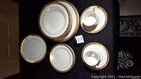 Top view of the full set including large plates, soup bowls, and teacup with saucer, all featuring gold decorative trim.