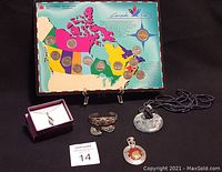 Canada 125 collector coin set displayed with multiple pieces of jewelry on a black surface. The coin set is mounted on a colorful geographic board of Canada highlighting provinces with coins.