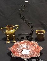 Front view of five decorative items including brass bell receptacle, candlesticks, spiral candleholder, flower plate, and small cup