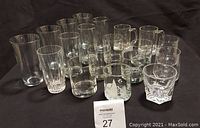 Set of 19 assorted clear drinking glasses displayed against a black background showing variety in sizes and styles.