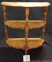 Three-tier solid wood corner shelf photographed against a black backdrop