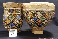 Front view of the two ceramic bongos connected by rope lacing with colorful geometric floral patterns on the ceramic body.