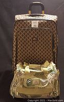 Photo of the luggage set showing a large patterned suitcase with a brown fleur-de-lis style design and a cream carry-on bag featuring a circular swirl pattern placed in front.