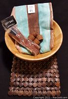 Wooden salad bowl holding folded striped tablecloths and napkin rings, with place setting mats arranged beneath bowl.
