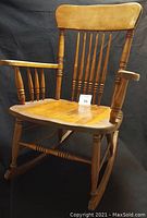 Front angled view of the antique hardwood rocking chair showing the spindle backrest, armrests, and seat.