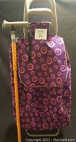Purple wheeled shopping cart with pink and orange circle pattern shown from front with tag attached.