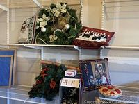 Photo of two Christmas wreaths and three decorative pillows arranged on shelves with folded Christmas fabric.