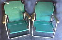 Two retro aluminum folding chairs placed side by side on floor. Turquoise vinyl seats and backs with cream plastic armrests visible.